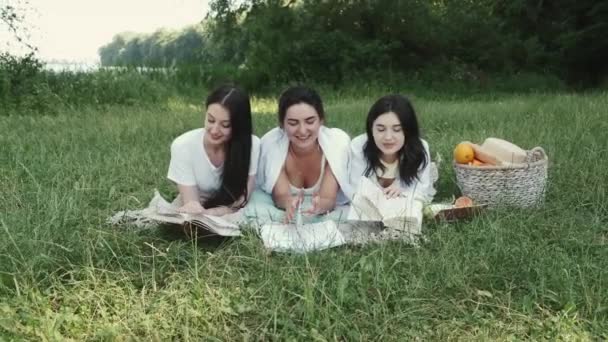 Trzy ładne dziewczyny leżą w trawie z książkami. — Wideo stockowe