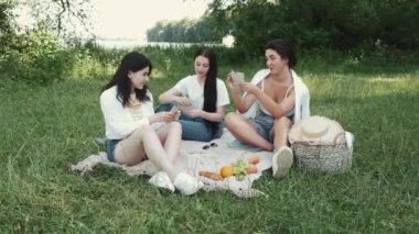 Bir grup kız arkadaş dışarıda piknik yapıyor ve kağıt oynuyor.