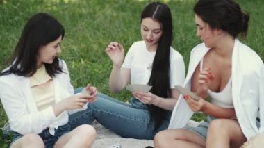 Bir grup kız arkadaş dışarıda piknik yapıyor ve kağıt oynuyor.