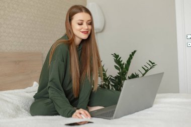 Yatakta oturan ve dizüstü bilgisayar kullanan bir kadın.