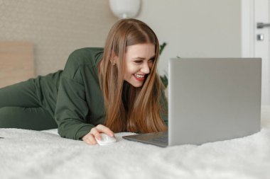 Yatakta oturan ve dizüstü bilgisayar kullanan bir kadın.