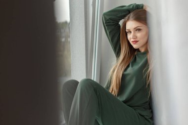 Evdeki pencere pervazında oturan kadın.