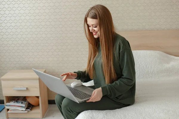 Yatakta oturan ve dizüstü bilgisayar kullanan bir kadın.