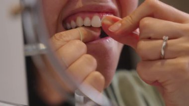 Bir kadın aynanın önünde dikilirken dişlerini temizlemek için diş ipi kullanıyor.