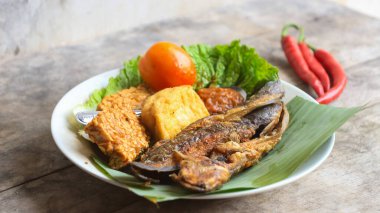 Domates soslu ve taze sebzeli bir tabak kızarmış yayın balığı geleneksel Endonezya mutfağıdır. catfish pecel, menü katalogları, yemek tarifi dergileri ve kapaklar için uygun