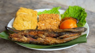 Domates soslu ve taze sebzeli bir tabak kızarmış yayın balığı geleneksel Endonezya mutfağıdır. catfish pecel, menü katalogları, yemek tarifi dergileri ve kapaklar için uygun