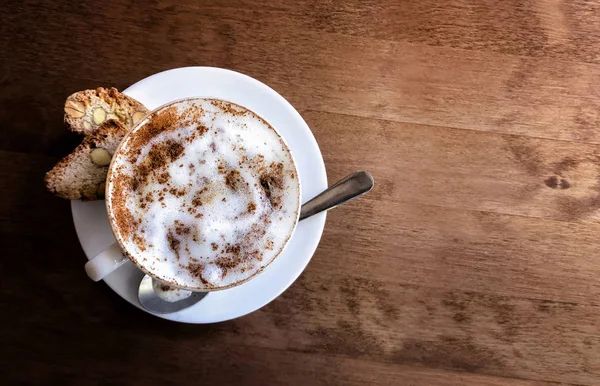 latte or cappuccino with frothy foam, cinnamon and nut cookies, top view of a cup of coffee on a wooden table in a cafe