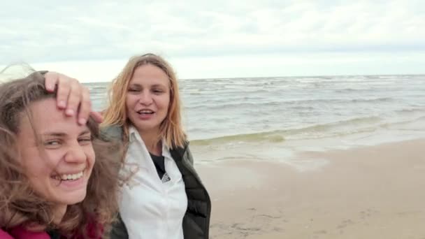 Två glada tjejer vandring längs stranden vintern och skjuter selfie. — Stockvideo