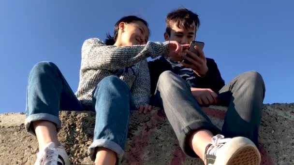 Dos adolescentes sentados en la calle y viendo videos divertidos en el teléfono . — Vídeo de stock