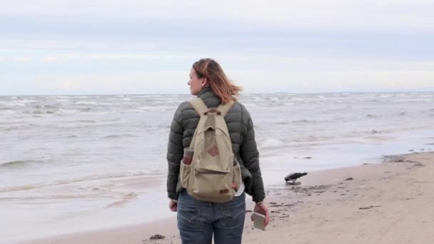 Jonge vrouw met een rugzak is een strand wandelen. — Stockvideo