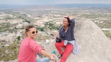 İki genç kadın yolcunun dağ ve Göreme city, Türkiye arka planda bir selfie alarak kenarına oturur.