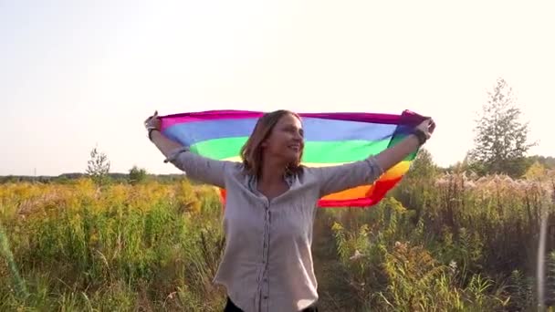 森の草原の真ん中に立って手で虹色の旗を持つ女性 — ストック動画