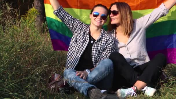 Twee Jonge Vrouwen Zitten Een Achtergrond Van Regenboogvlag Zon Schijnt — Stockvideo