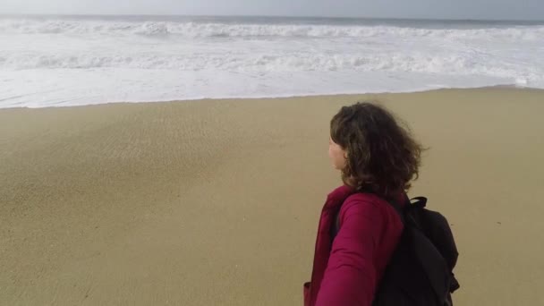 Eine junge Frau mit einem Rucksack macht ein Selfie im Hintergrund des Ozeans. — Stockvideo