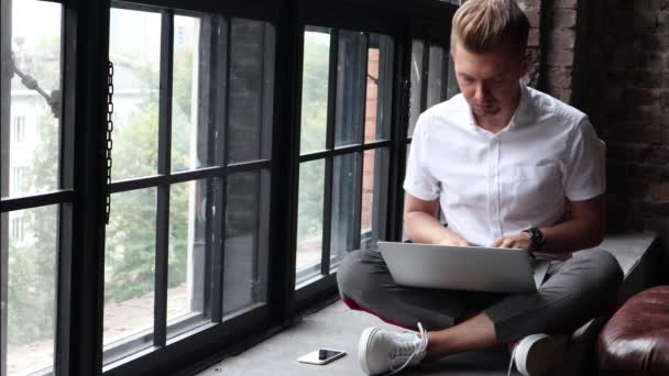 Ένας Νεαρός Άνδρας Κάθεται Ένα Windowsill Και Λειτουργεί Χρησιμοποιώντας Ένα — Αρχείο Βίντεο