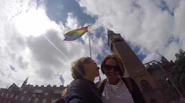 Genç bir gay çift hareketli gökkuşağı bayrağı arka üzerinde öpüyor.