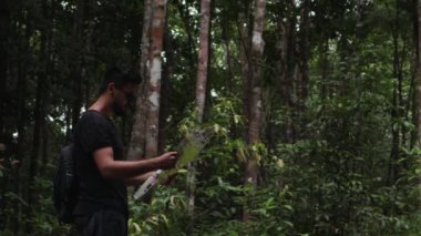 Bir harita kullanarak tropikal ormanlarda, doğru yolu arayan genç adam.