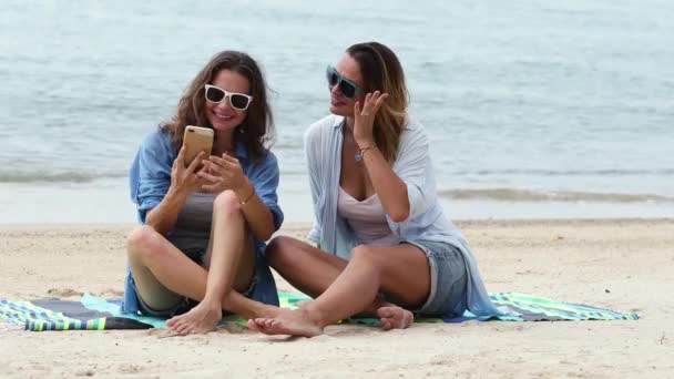 Twee jonge vrouwen nemen een selfie met een telefoon op het strand op een zonnige dag. — Stockvideo