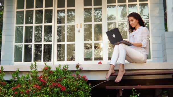 Een mooie jonge vrouw zit op de veranda met een laptop. — Stockvideo