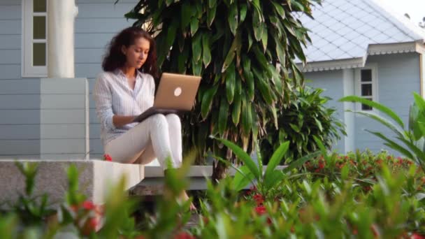 En ung vacker kvinna sitter på verandan med en bärbar dator. — Stockvideo