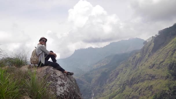 Woman traveler is sitting on the big rock in the mountain. — Stock Video