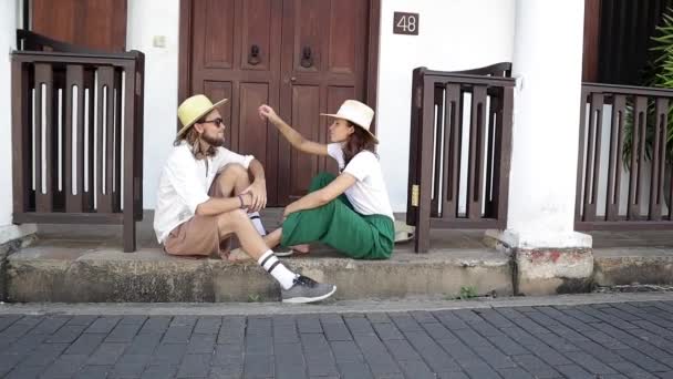 Joven pareja con estilo en sombreros de paja está sentado en la puerta . — Vídeos de Stock