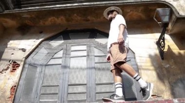 Hasır şapkalı ve güneş gözlükçü genç bir adam eski tarihi bir evin dar kaldırımında denge kurmaya çalışıyor..