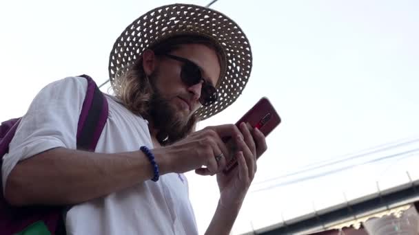 Молодой Человек Соломенной Шляпе Солнечных Очках Пользуется Своим Смартфоном Улице — стоковое видео