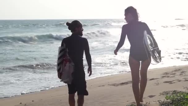 Deux jeunes marchent avec une planche de surf sur la plage au coucher du soleil . — Video