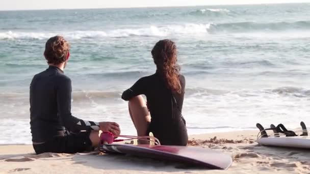 Um jovem casal de surfistas está a descansar na praia. — Vídeo de Stock