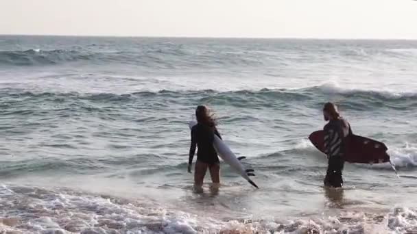 Um jovem casal de surfistas vai para o oceano com as suas pranchas de surf. . — Vídeo de Stock