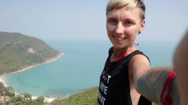 Kısa saçlı Genç hipster kadın güzel bir deniz manzarası ile uçurumun kenarında duran ve bir selfie alarak.