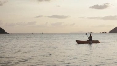 Elinde bir kürek ile genç bir kadın günbatımı zamanında denizde bir kayık üzerinde yüzen.