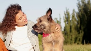 Uzun kıvırcık saçlı mutlu genç beyaz kadın yaz aylarında parkta köpeği ile iyi vakit geçiriyor.