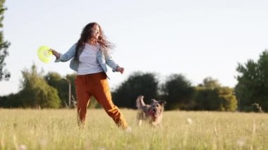 Uzun kıvırcık saçlı mutlu genç beyaz kadın parkta köpeği ile oynuyor. 