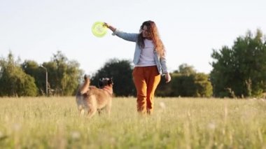 Uzun kıvırcık saçlı mutlu genç beyaz kadın parkta köpeği ile oynuyor. 