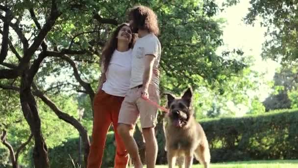 Молодая красивая любящая пара, гуляющая в парке со своей собакой — стоковое видео