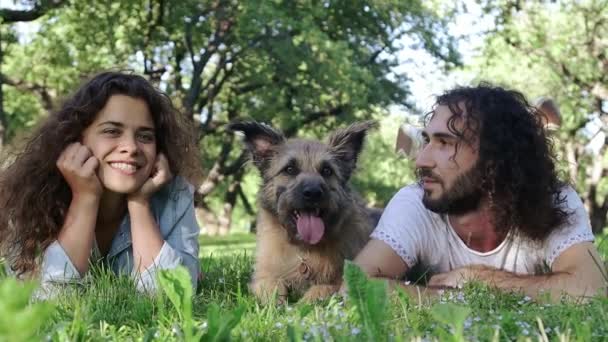 Mladý veselý párek ležící na trávě v parku se svým psem. — Stock video