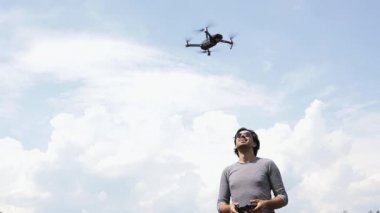 Güneş gözlüklü genç yakışıklı bir adam uzaktan kumandalı uçan bir dronu izliyor ve yönlendiriyor..  