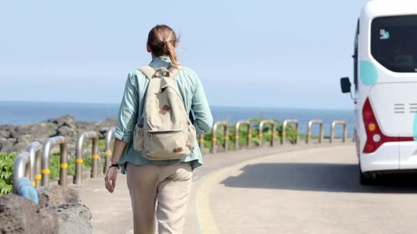 Молодая женщина туристка с рюкзаком прогулка по дороге с видом на море . — стоковое видео