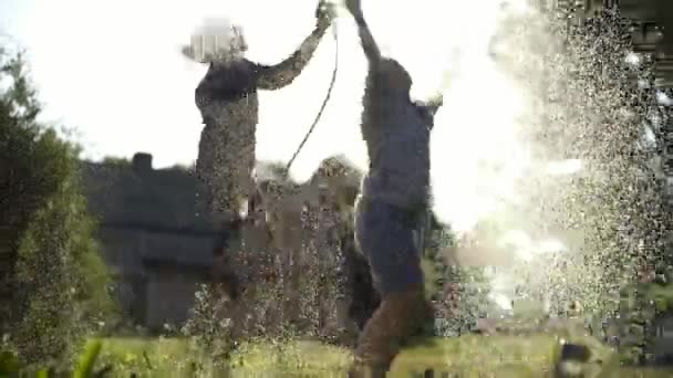 Joven pareja alegre manguera del jardín y jugando bajo aerosoles de agua — Vídeo de stock