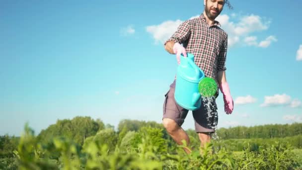 Ung stilig hipster man vattning trädgården med ett land vattning kan. — Stockvideo