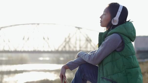 Aziatische mixed-race brunette tiener meisje luisteren naar muziek met haar koptelefoon — Stockvideo