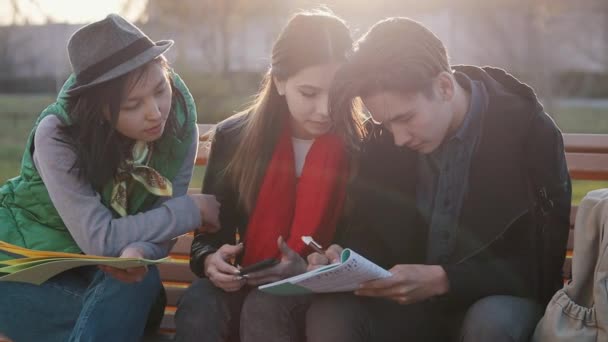 Tres adolescentes asiáticos haciendo deberes en el parque al atardecer — Vídeos de Stock
