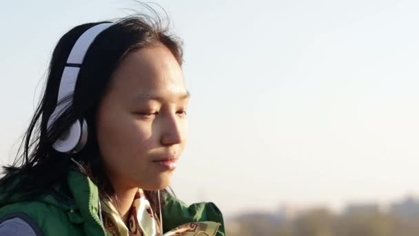 Азиатская брюнетка смешанной расы, слушающая музыку в наушниках — стоковое видео