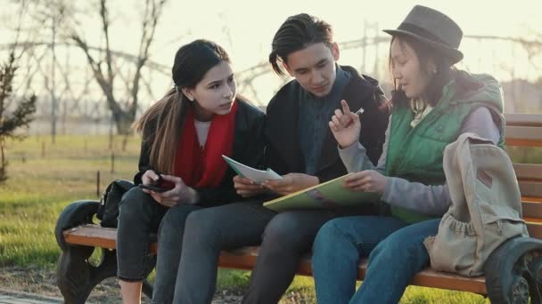 Üç Asyalı genç gün batımında parkta ev ödevi yapıyor. — Stok video