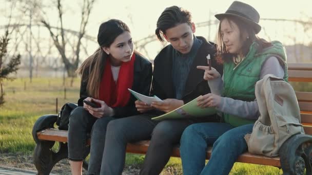 日没時に公園で宿題をしている3人のアジアのティーンエイジャー. — ストック動画