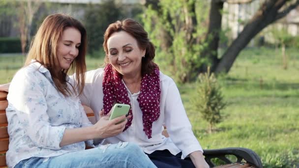 Two attractive happy old and middle-aged women girlfriends using a smartphone — Stock Video