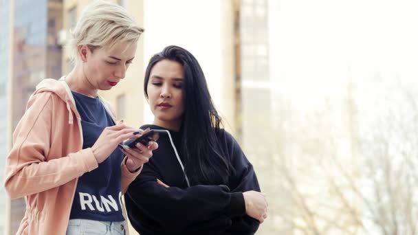 Dos mujeres jóvenes de diferentes nacionalidades, amigos multiétnicos usando un teléfono inteligente — Vídeos de Stock