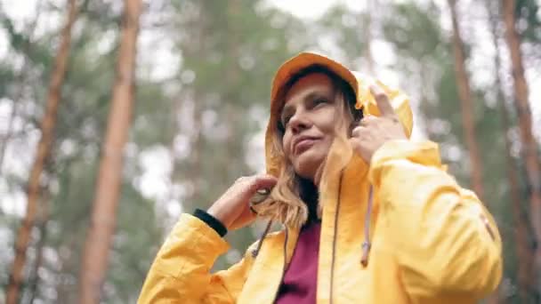 Retrato de una mujer joven con una chaqueta de color amarillo brillante de pie en el bosque lluvioso — Vídeo de stock